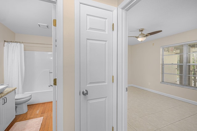 full bathroom with vanity, hardwood / wood-style flooring, shower / bath combo with shower curtain, toilet, and ceiling fan