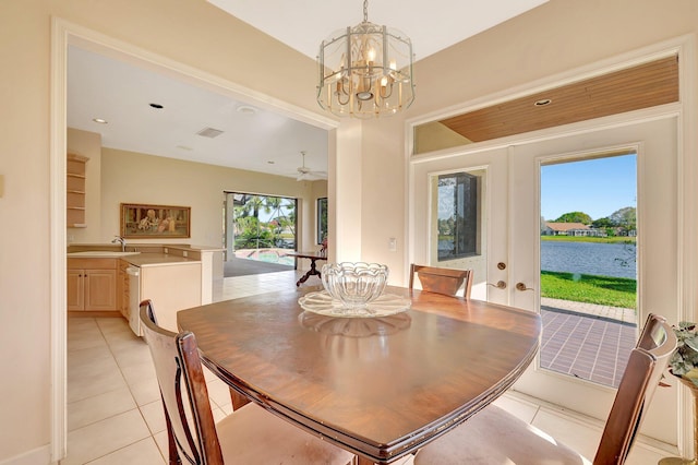 dining area featuring french doors, sink, a water view, an inviting chandelier, and light tile patterned floors