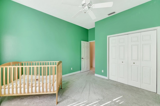 unfurnished bedroom featuring a crib, light colored carpet, ceiling fan, and a closet