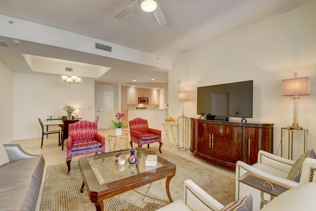 tiled living room with ceiling fan with notable chandelier and a tray ceiling