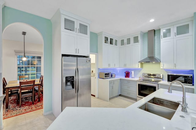 kitchen featuring white cabinetry, sink, hanging light fixtures, stainless steel appliances, and wall chimney range hood