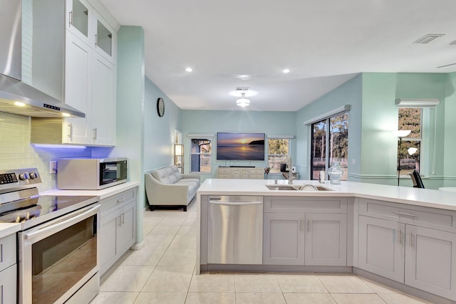 kitchen featuring light tile patterned flooring, wall chimney exhaust hood, sink, tasteful backsplash, and appliances with stainless steel finishes