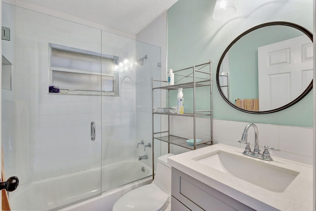 full bathroom featuring tile walls, bath / shower combo with glass door, vanity, a textured ceiling, and toilet