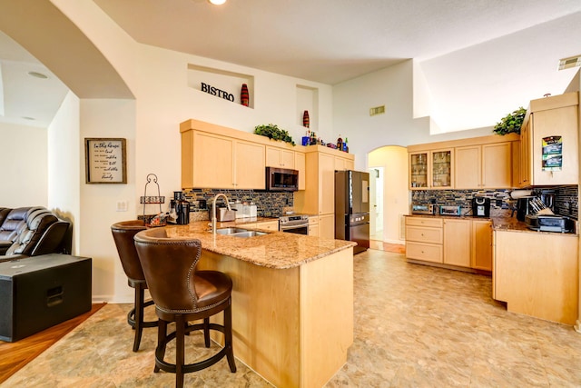 kitchen with sink, appliances with stainless steel finishes, light stone counters, light brown cabinetry, and kitchen peninsula