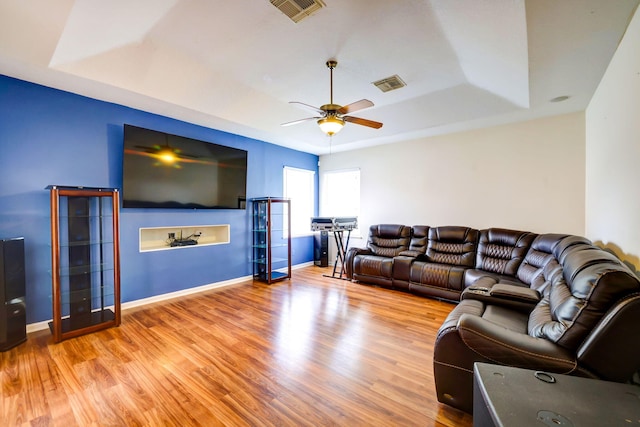 living room with ceiling fan, a raised ceiling, and light hardwood / wood-style flooring