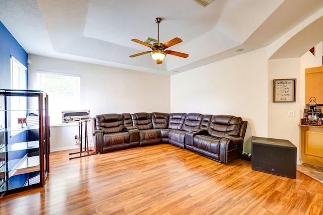 living room with ceiling fan, light hardwood / wood-style floors, and a tray ceiling