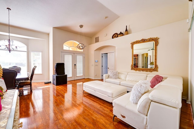 living room with hardwood / wood-style flooring, high vaulted ceiling, an inviting chandelier, and french doors