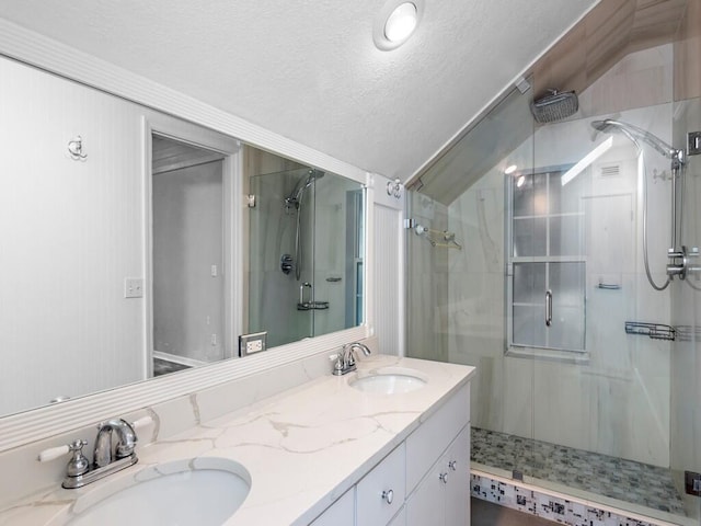 bathroom with a shower with shower door, vanity, vaulted ceiling, and a textured ceiling