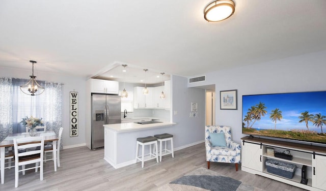 kitchen featuring white cabinets, a kitchen breakfast bar, hanging light fixtures, stainless steel fridge, and kitchen peninsula