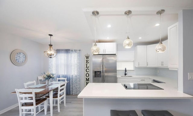 kitchen featuring decorative light fixtures, a breakfast bar, stainless steel refrigerator with ice dispenser, kitchen peninsula, and white cabinets