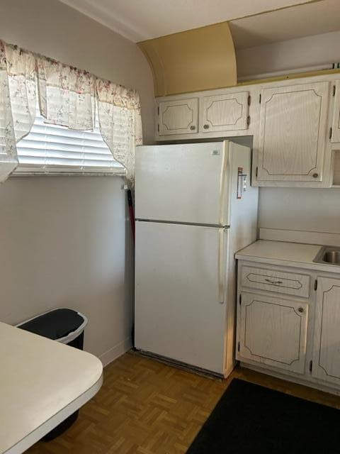 kitchen featuring white fridge, white cabinetry, light parquet flooring, and sink