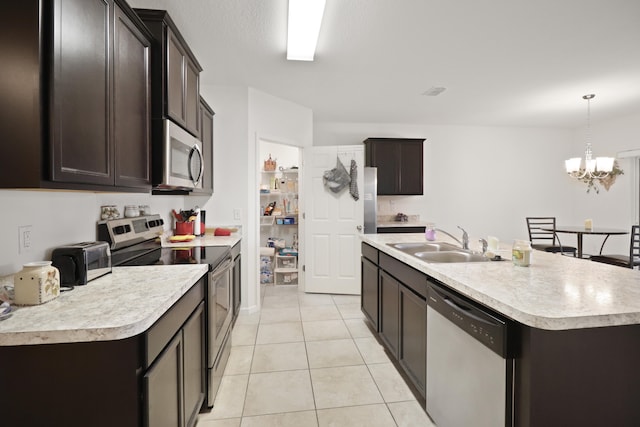 kitchen featuring decorative light fixtures, sink, light tile patterned floors, stainless steel appliances, and a center island with sink