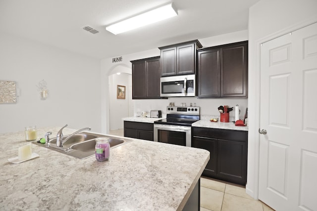 kitchen with dark brown cabinetry, sink, light tile patterned flooring, and appliances with stainless steel finishes