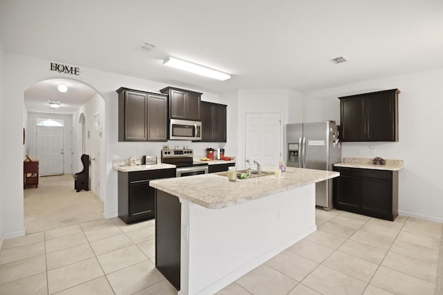 kitchen featuring light tile patterned flooring, an island with sink, sink, stainless steel appliances, and dark brown cabinets