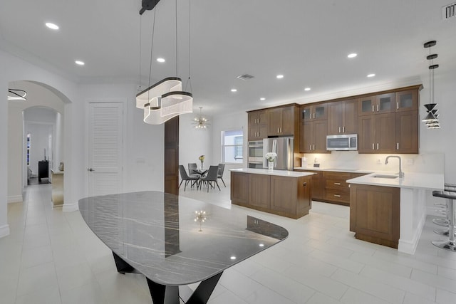 kitchen with visible vents, a center island, arched walkways, stainless steel appliances, and a sink