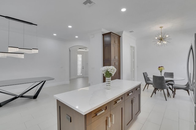 kitchen featuring visible vents, a center island, ornamental molding, arched walkways, and a notable chandelier