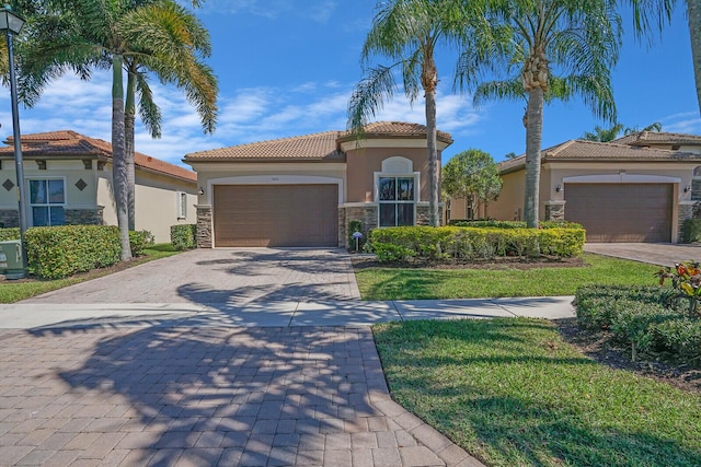 mediterranean / spanish house with a front yard, an attached garage, stucco siding, stone siding, and decorative driveway