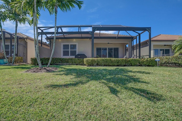 back of house with stucco siding, a lawn, glass enclosure, and a ceiling fan