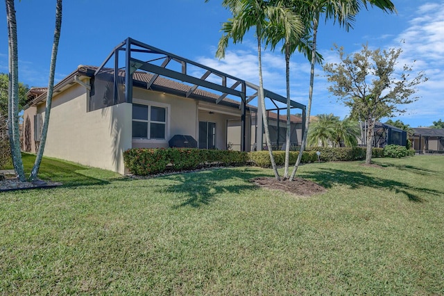 rear view of house with a lanai, a yard, and stucco siding