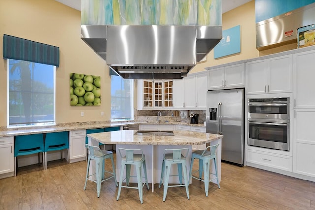 kitchen featuring tasteful backsplash, a breakfast bar, appliances with stainless steel finishes, white cabinets, and wall chimney exhaust hood