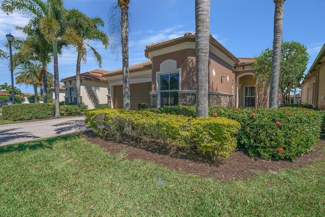 view of front of home with a front yard, an attached garage, stucco siding, a tile roof, and decorative driveway