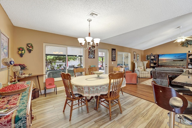 dining space with a textured ceiling, lofted ceiling, and ceiling fan with notable chandelier