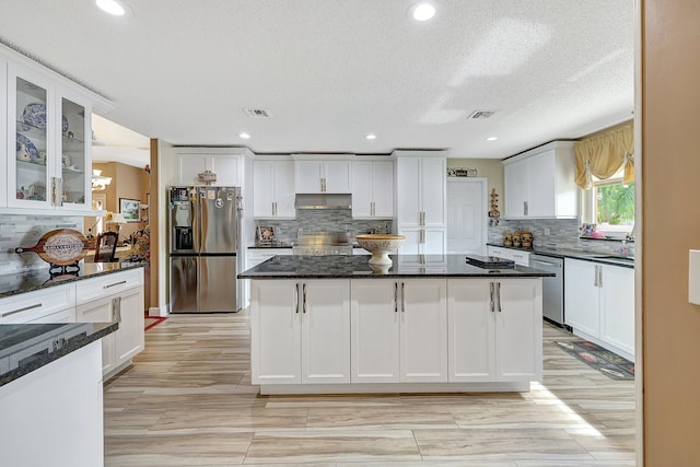 kitchen featuring dark stone countertops, a kitchen island, white cabinetry, appliances with stainless steel finishes, and a textured ceiling