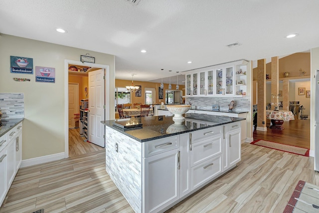 kitchen featuring a kitchen island, white cabinetry, dark stone countertops, decorative backsplash, and hanging light fixtures