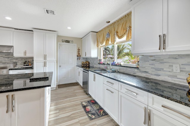 kitchen featuring wall chimney range hood, white cabinetry, dark stone counters, sink, and stainless steel dishwasher