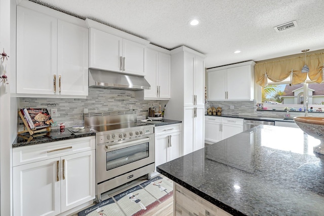 kitchen featuring a textured ceiling, white cabinetry, stainless steel appliances, dark stone counters, and backsplash