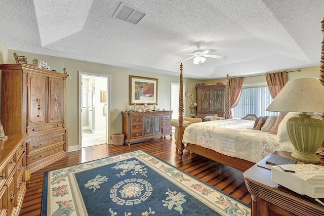 bedroom with ceiling fan, ensuite bathroom, a raised ceiling, dark wood-type flooring, and a textured ceiling