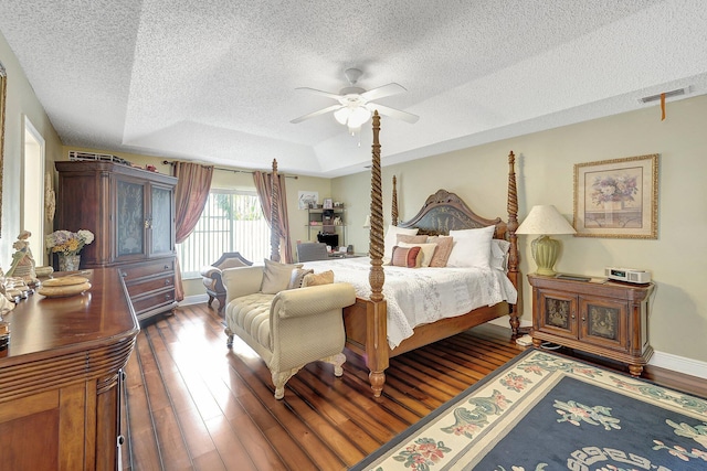 bedroom with ceiling fan, hardwood / wood-style floors, a tray ceiling, and a textured ceiling