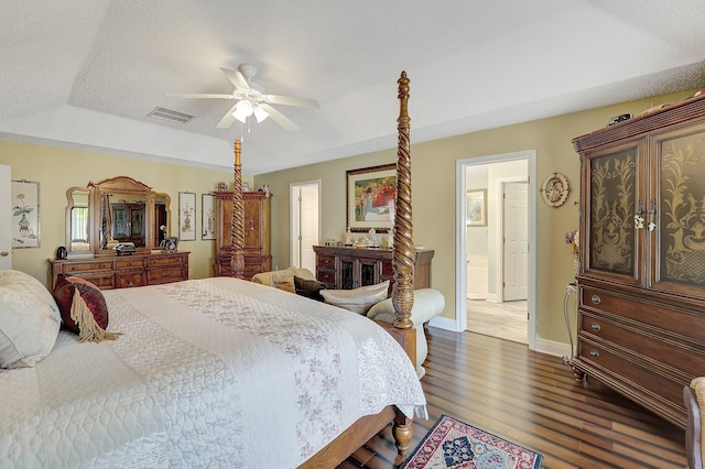 bedroom with dark wood-type flooring, ceiling fan, a tray ceiling, and ensuite bath