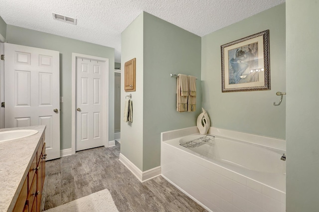 bathroom with a bath, a textured ceiling, wood-type flooring, and vanity