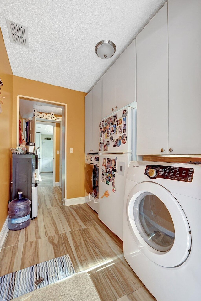 clothes washing area with washer and dryer, cabinets, and a textured ceiling