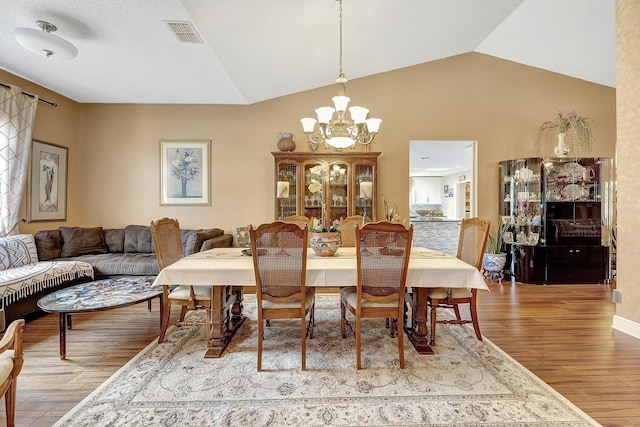 dining area with light wood-type flooring, vaulted ceiling, and a notable chandelier