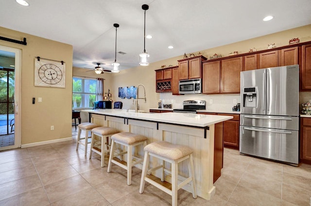 kitchen with sink, pendant lighting, appliances with stainless steel finishes, and a kitchen island with sink