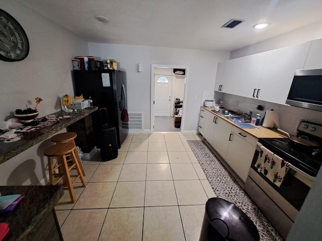 kitchen with appliances with stainless steel finishes, white cabinetry, light tile patterned flooring, and backsplash