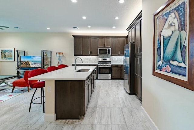 kitchen with appliances with stainless steel finishes, a kitchen bar, decorative backsplash, sink, and a center island with sink