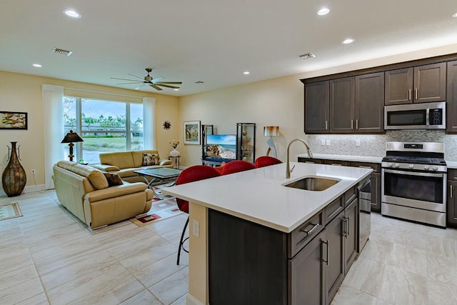 kitchen featuring dark brown cabinets, appliances with stainless steel finishes, sink, a center island with sink, and decorative backsplash