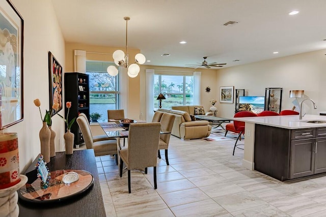 dining area with ceiling fan with notable chandelier and sink