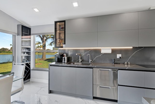 kitchen featuring sink, a water view, dark stone countertops, gray cabinets, and backsplash