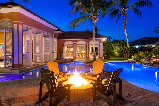 pool at night featuring an outdoor structure, a patio area, and an outdoor fire pit