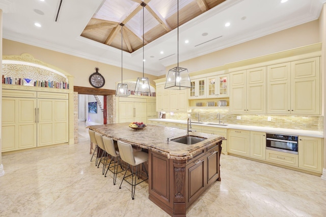 kitchen with sink, a center island with sink, oven, and cream cabinetry