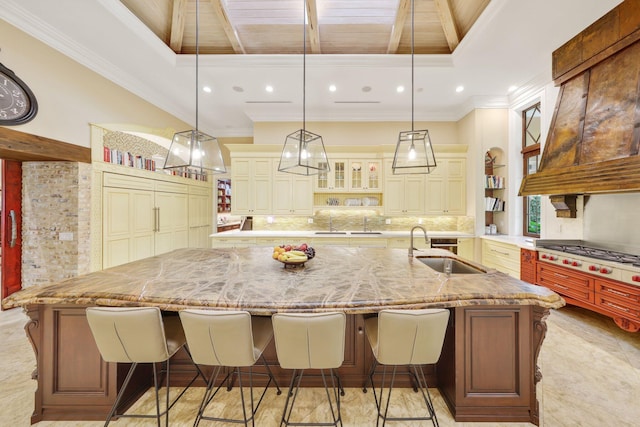 kitchen featuring a spacious island, stainless steel gas cooktop, sink, light stone counters, and decorative light fixtures