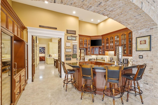 kitchen featuring backsplash, a kitchen bar, kitchen peninsula, and a high ceiling