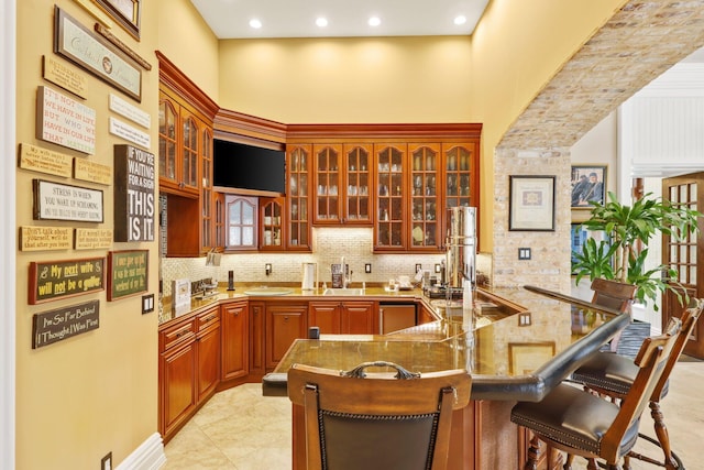 kitchen featuring stone counters, a breakfast bar, sink, a high ceiling, and kitchen peninsula