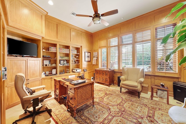 home office with crown molding, built in shelves, ceiling fan, and wood walls