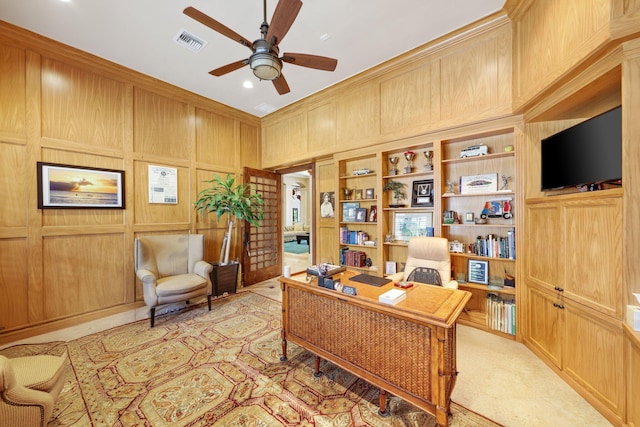 office with built in shelves, ceiling fan, and wood walls