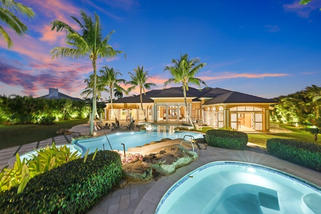 pool at dusk with an in ground hot tub and a patio